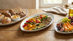 Plates of grilled vegetables, bread, and fruit on a wooden table.