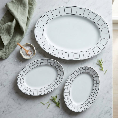 Set of three white plates with black geometric patterns on a marble surface.