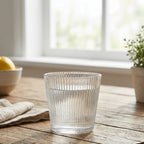 Clear glass of water on a wooden table with lemons and a plant in the background