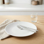 White plate with silverware on a wooden table with a glass of water.