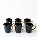 Set of six black mugs with gold handles on a white background