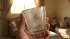 Hand holding a clear glass with ribbed texture indoors