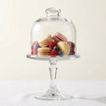 Glass dome on a pedestal with assorted cookies and berries inside, on a white background
