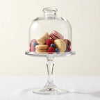 Glass dome on a pedestal with assorted cookies and berries inside, on a white background