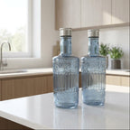 Two blue glass bottles on a kitchen counter with a window and cabinets in the background.