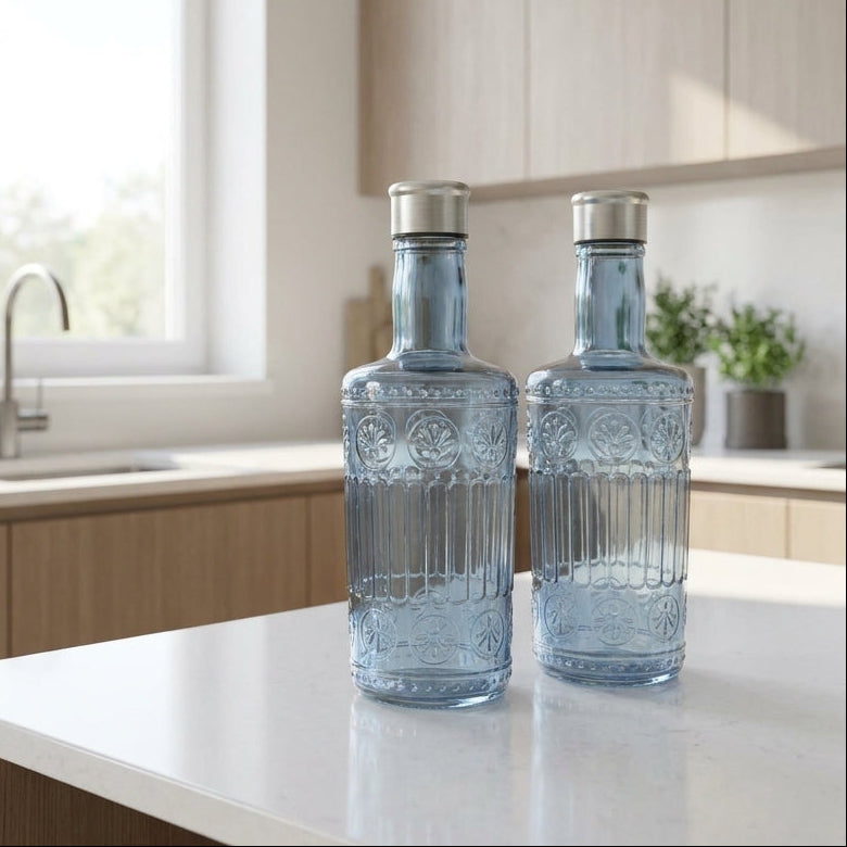 Two blue glass bottles on a kitchen counter with a window and cabinets in the background.