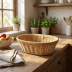Wicker basket on a wooden table with a bowl of fruit and plants in the background.