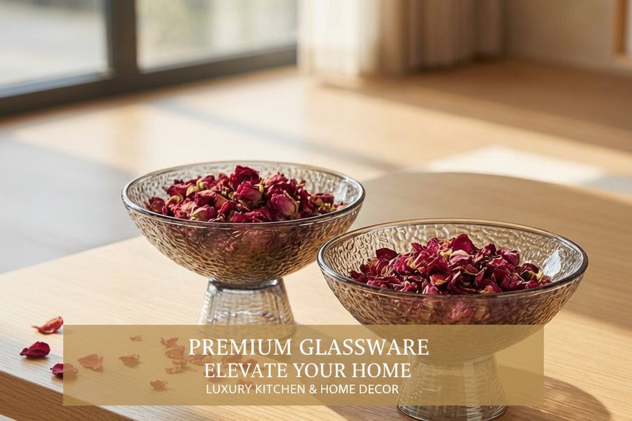 Two glass bowls with dried flowers on a wooden table near a window.
