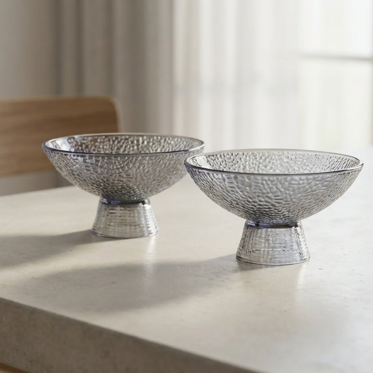 Two silver decorative bowls on a light-colored table with a blurred background