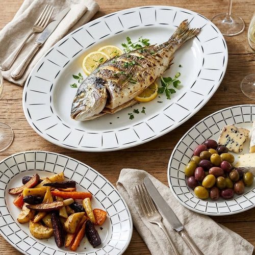 Dinner table setting with grilled fish, roasted vegetables, and olives.