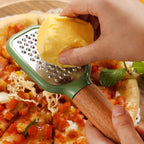 Person grating cheese onto a pizza with a green and wooden grater.