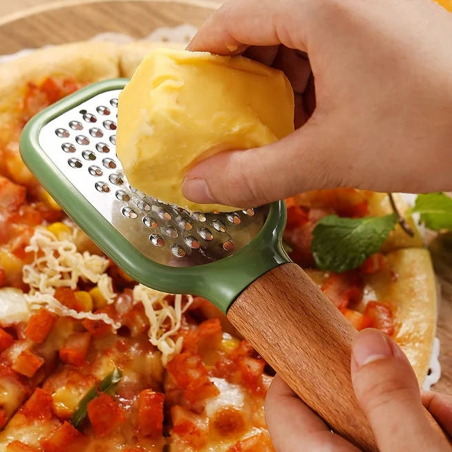 Person grating cheese onto a pizza with a green and wooden grater.