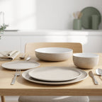 Dining table set with beige plates, bowls, and silverware on a wooden table.