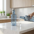 Person pouring water from a bottle into a glass in a kitchen.
