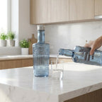 Person pouring water from a bottle into a glass in a kitchen.