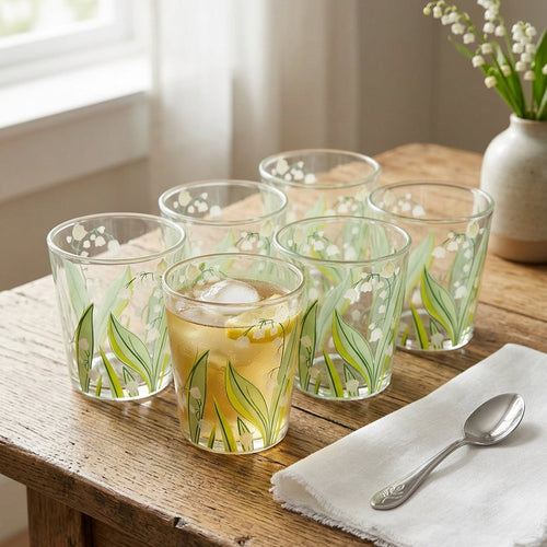 Set of glass tumblers with floral design on a wooden table with a vase of flowers in the background.