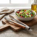 Bowl of salad with tongs on a wooden cutting board