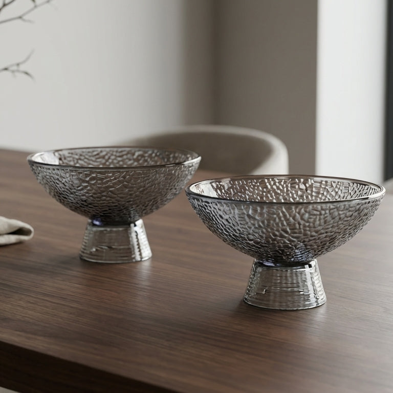 Two metallic bowls on a wooden table with a vase and napkin in the background.