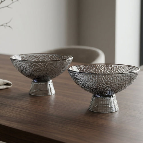Two metallic bowls on a wooden table with a vase and napkin in the background.
